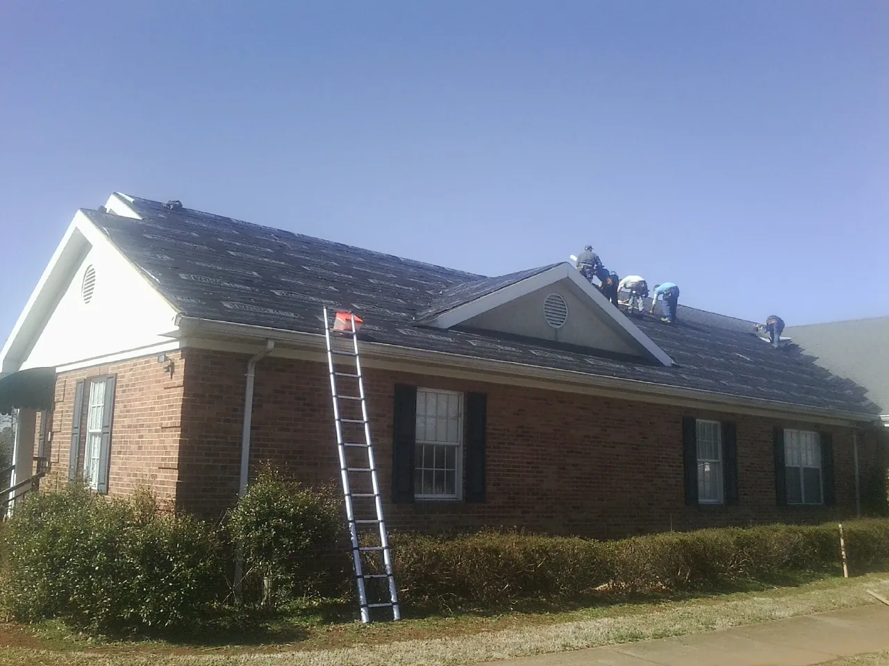 Crew tearing shingles off a brick ranch roof with a ladder set — Emergency Roof Repair work by our crew in Days Creek