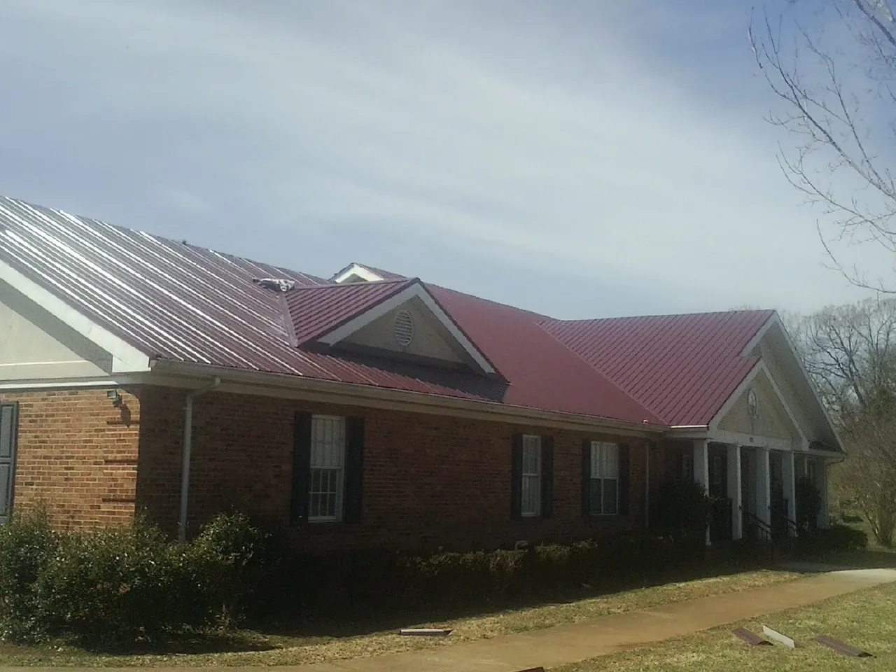 Red metal roof with gabled entries on a long brick building, from a Hail Damage Roof Repair job in Days Creek