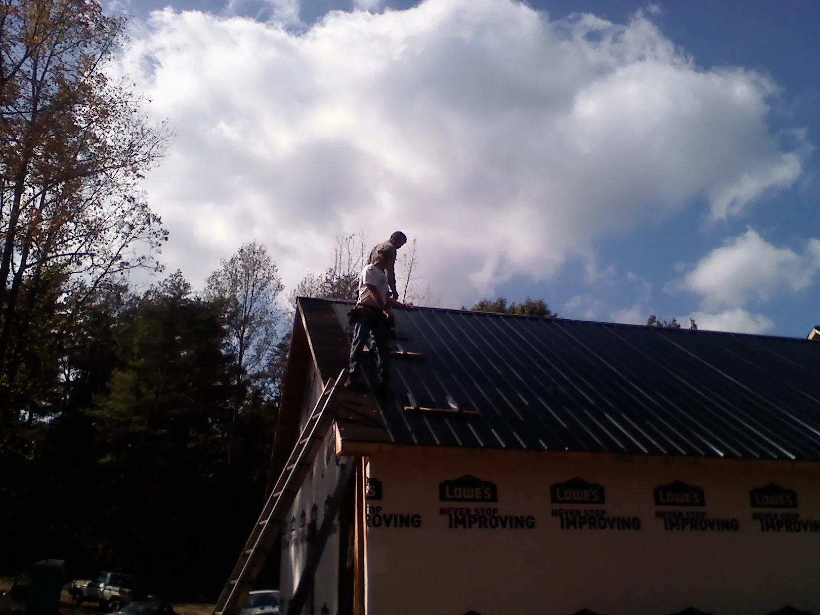 Roofer fastening dark metal panels high against a cloudy sky, from a Roof Inspection job in Days Creek