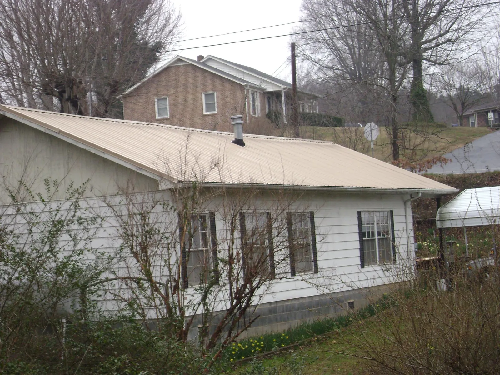 Tan metal roof on a white sided house set into a hillside — Commercial Roofing by Roofing Brothers in Days Creek